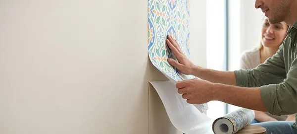 a lady trying to apply a peel-and-stick wallpaper on the wall