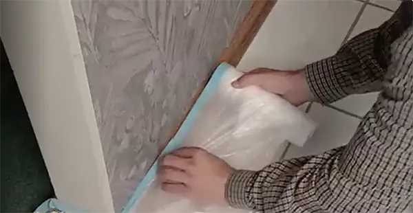 a person's hand applying a plastic sheet on the corner of the wall