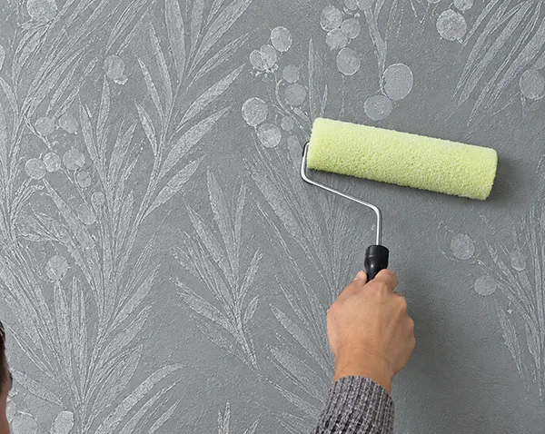 a person’s hand applying some solution on the wall with a paint roller