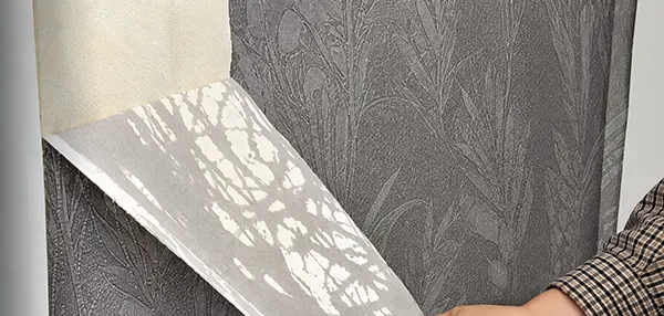 a person’s hand peeling the wallpaper from the wall