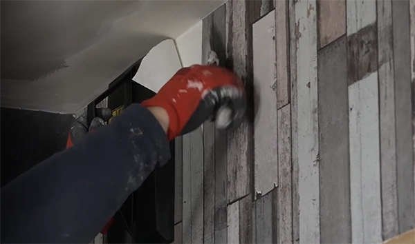 a person’s hand scraping the wallpaper using the putty knife with the other hand holding the water steamer on the wall